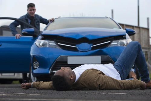 A man is lying in front of a car after a pedestrian accident.