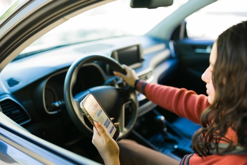 Distracted driver looking at her phone behind the wheel illustrating dangerous behavior linked to Uber and rideshare accidents.