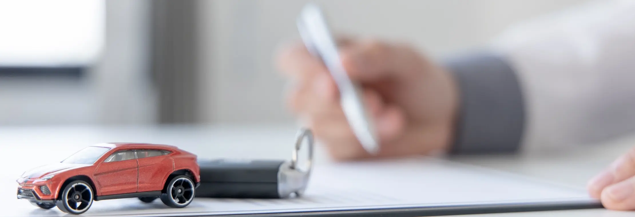 A person is holding a smartphone at a desk with orange and silver toy cars on documents representing a car accident in Knoxville, an insurance claim scenario.